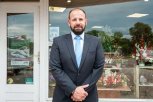Portrait du responsable des pompes funèbres devant la vitrine du magasin.