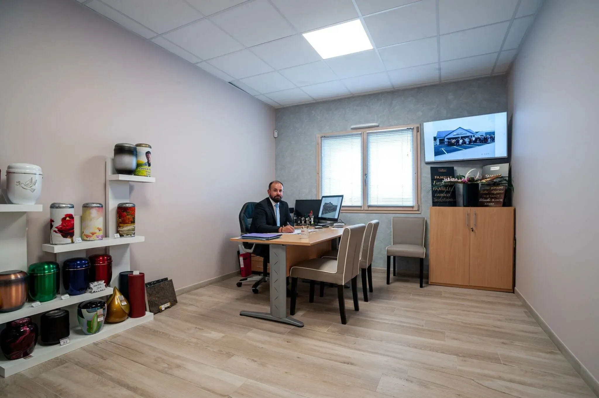 Conseiller funéraire assis à son bureau devant des étagères d'urnes.